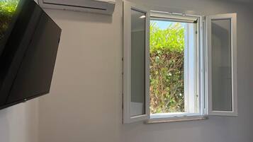 A room with a white wall, a window with white shutters, and an air conditioning unit.