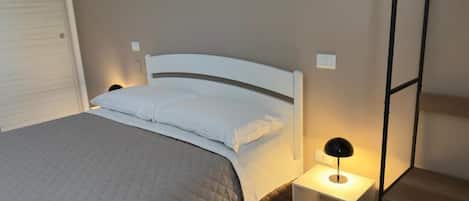 Una cama bien hecha con cubrecama acolchado, una lámpara de noche y una mesita de noche.