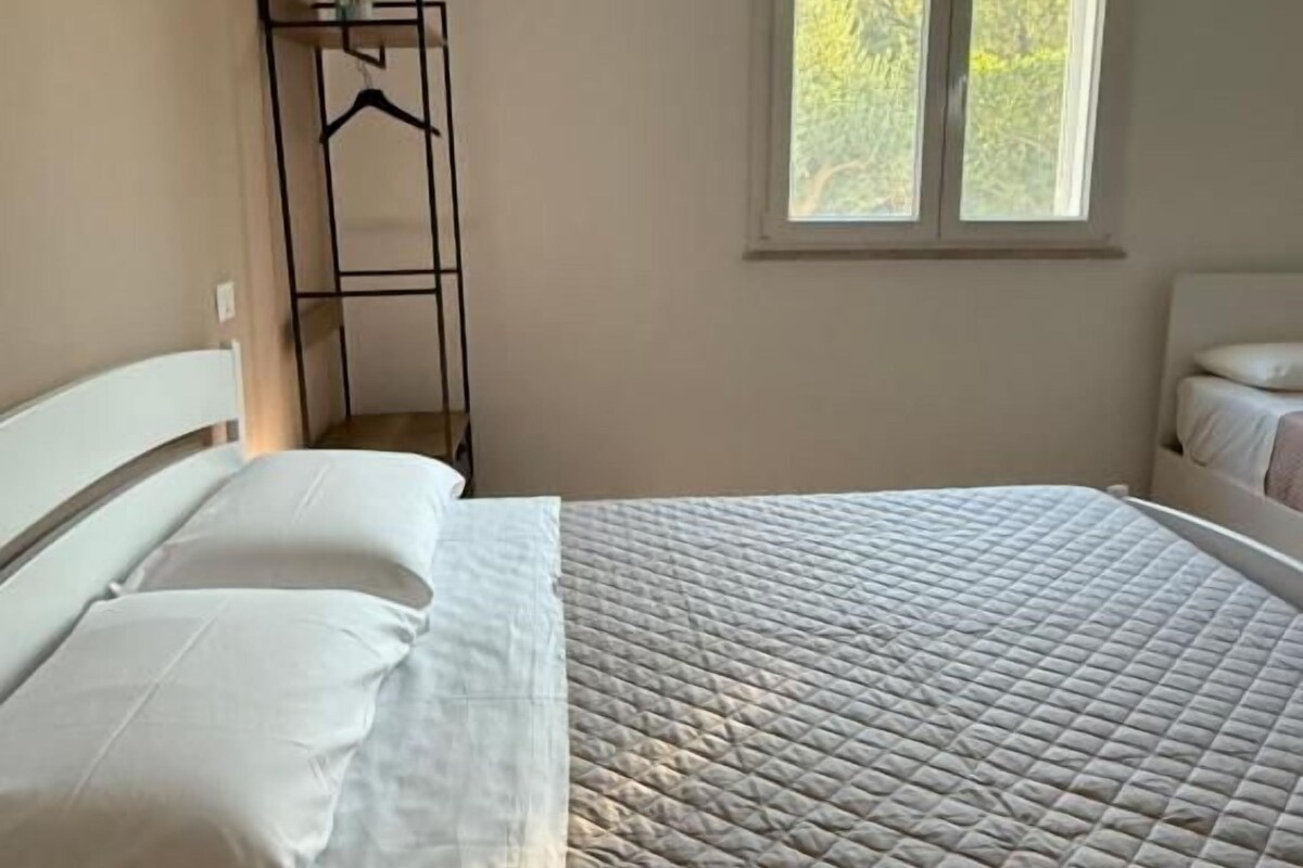 A bedroom with a bed, a window, and a bedside table.