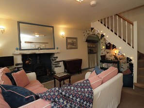 A living room with a fireplace, a staircase, and a cozy seating area. - Corner Cottage (Ulverston)