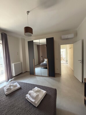 Een moderne slaapkamer met een groot bed, een spiegel, een radiator en uitzicht op een andere kamer.
