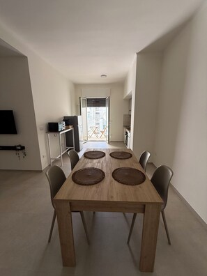 Een eetgedeelte met een houten tafel en vier stoelen, een televisie aan de muur en uitzicht buiten door een deur.