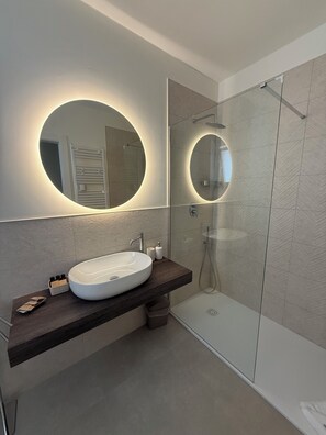 Een moderne badkamer met een groot ovaal wastafel, een spiegel met geïntegreerde verlichting en een douche met glazen wanden.