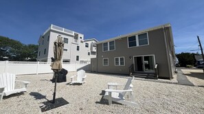A building with a covered outdoor seating area, white Adirondack chairs, and a gravel ground. - SPRAY BEACH OCEAN SIDE HOME (Spray Beach)
