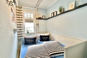 Ein Schlafzimmer mit einem Bett, gestreifte Kissen, einer Ablage mit Dekoration und einem Fenster mit Vorhängen.