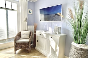 A room with a wicker chair, a white cabinet, a framed picture, and a potted plant. - Ostseeperle-3, prime location, south-facing balcony, parking space, close to the beach (Kühlungsborn)