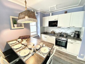 A modern kitchen with white cabinets, a built-in oven, and a dining area set with plates and cups. - Ostseeperle-3, prime location, south-facing balcony, parking space, close to the beach (Kühlungsborn)