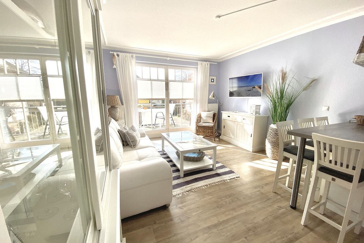 A modern living room with a white sofa, a coffee table, and a dining area with a table and chairs.