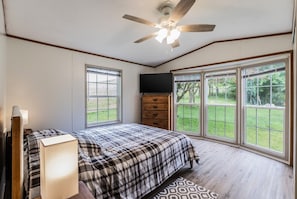 Un dormitorio con cama, cómoda, televisor y ventanas amplias con vistas al exterior.