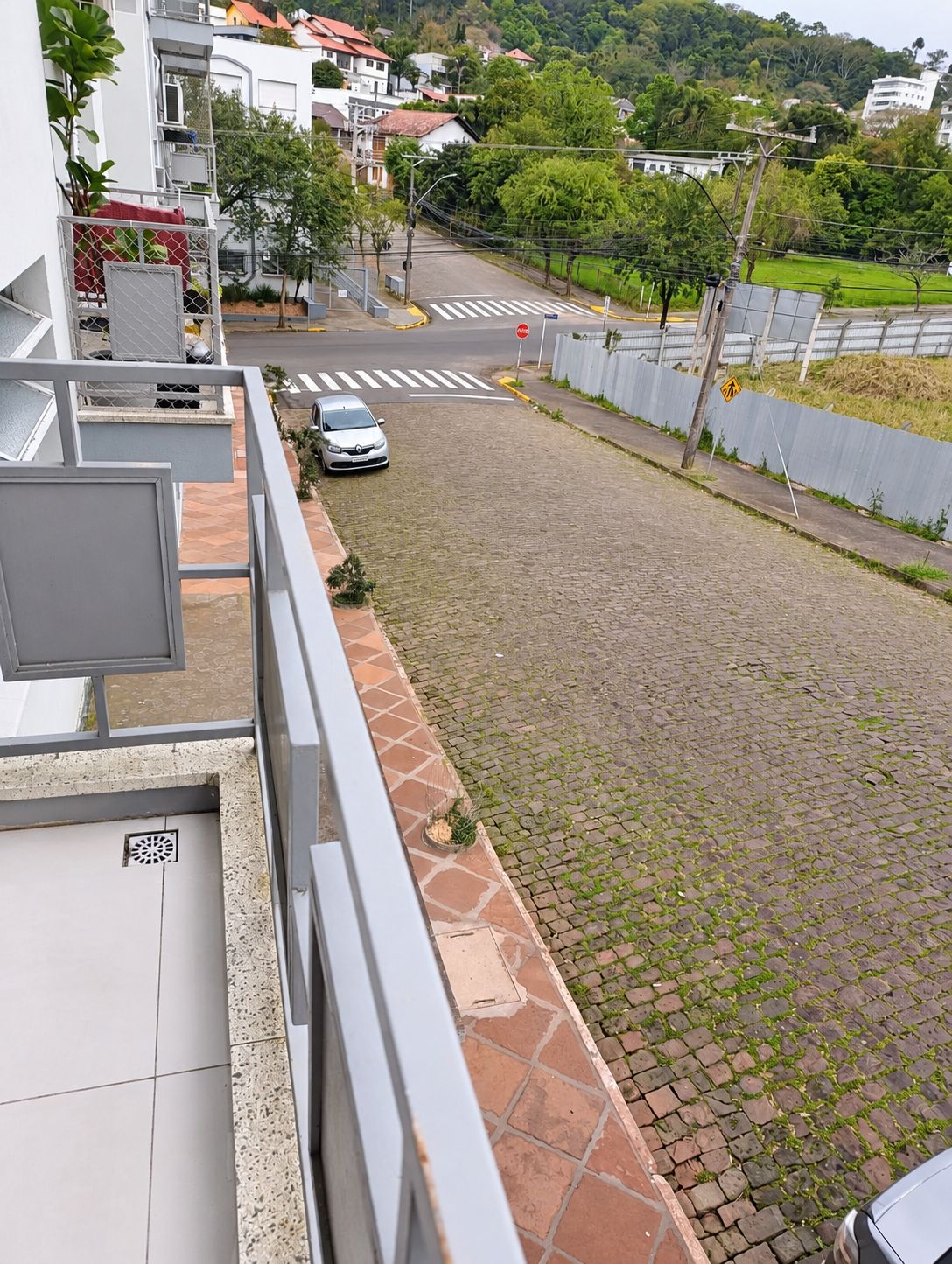 Un quartier résidentiel avec une allée pavée, une voiture garée et un passage piéton.