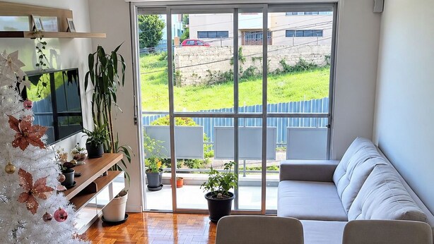 A modern living room with a white sofa, a dining table, and a large window with a view of a green landscape. -  APTO  CENTRAL PARA PASSEIO, A TRABALHO,  VISITAR FAMILIARES EM  STA CRUZ DO SUL (Santa Cruz do Sul)
