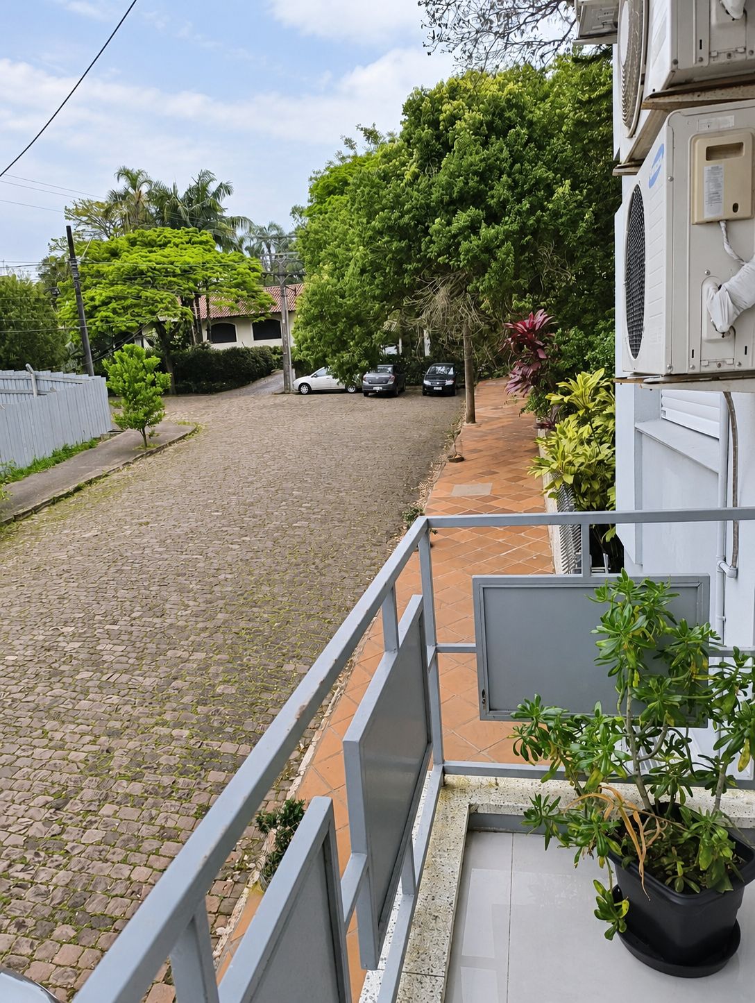 Un patio empedrado con un sendero pavimentado, una cerca blanca y una fila de coches aparcados.