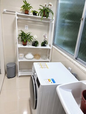 A laundry area with a washing machine, a drying rack, and shelves with potted plants.