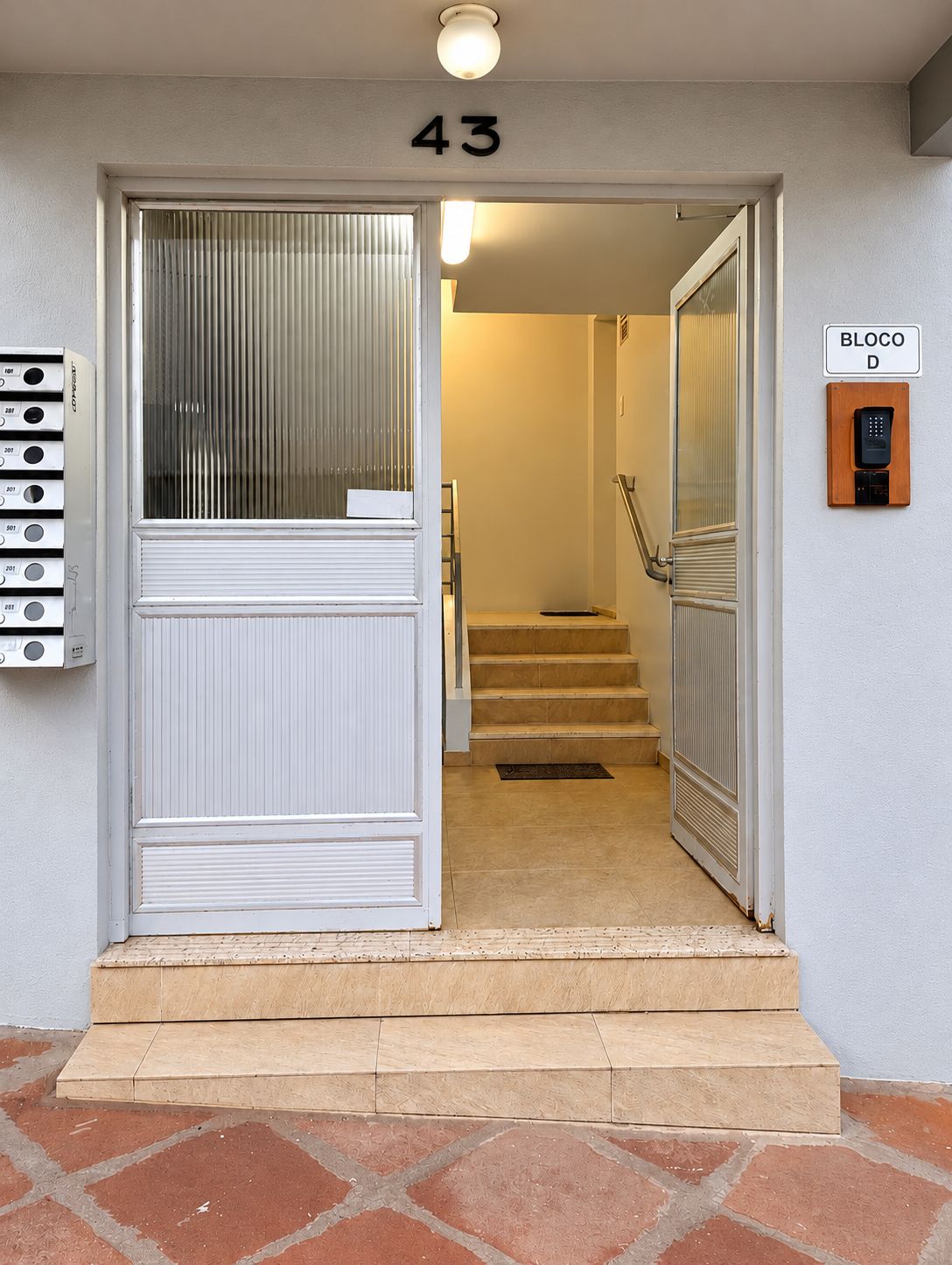 Una entrada de edificio con el número '43' sobre la puerta, un teclado de seguridad y una escalera que conduce al interior.