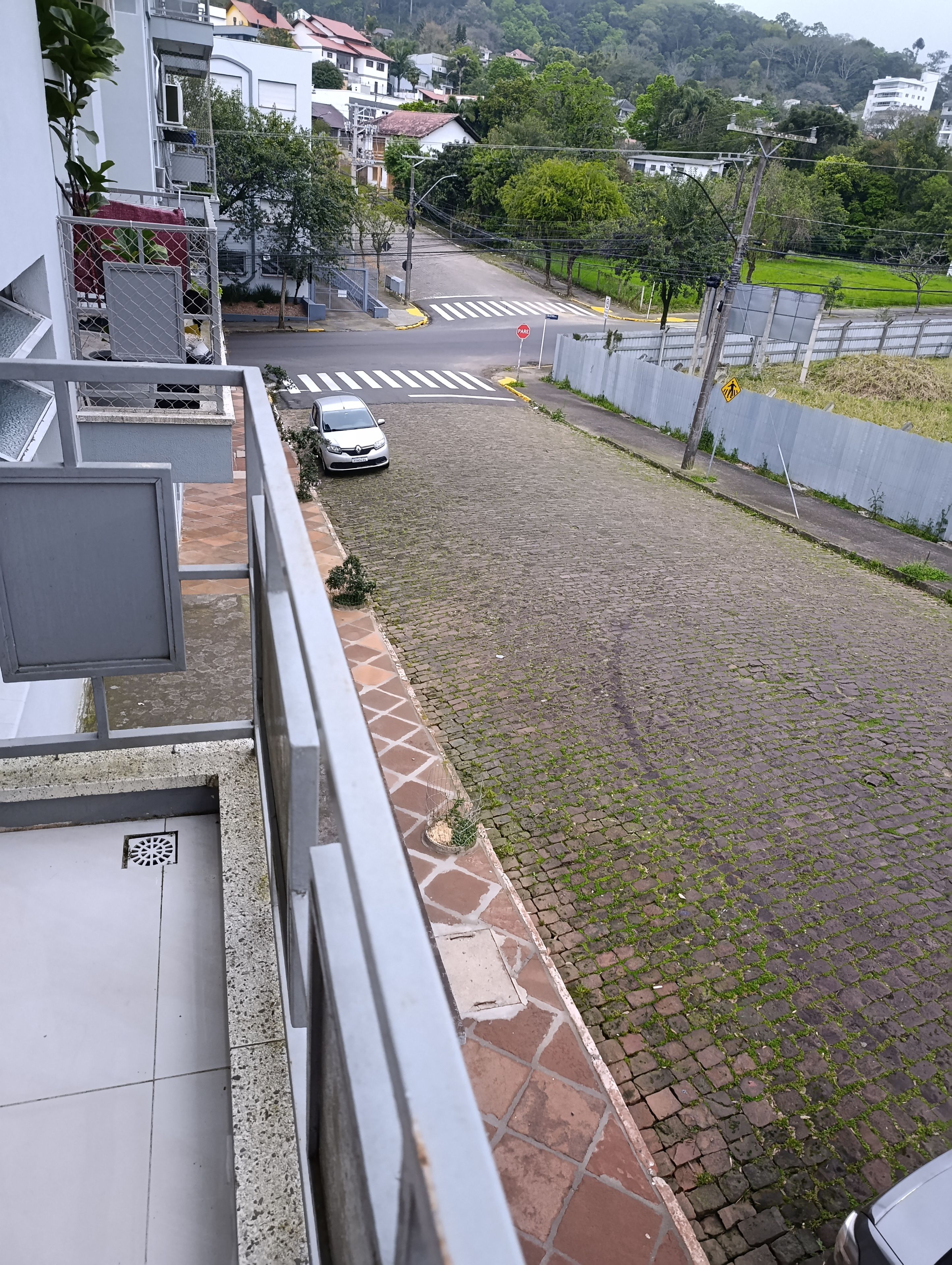 Área residencial com rua pavimentada, faixa de pedestres e um carro estacionado.