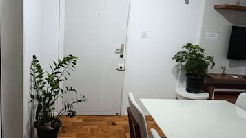 Una habitación con piso de madera en patrón de espiga, una puerta blanca, una mesa de comedor con sillas y dos plantas en macetas.