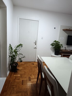 A room with a wooden herringbone floor, a white door, a dining table with chairs, and two potted plants.