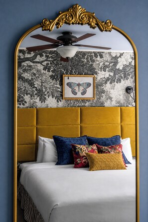 Een slaapkamer met een gestoffeerd hoofdeinde, een plafondventilator en een wanddecoratie met een vlinder.