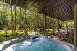 Een hottub onder een houten pergola, met een bos op de achtergrond.