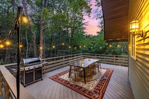 Een terras met een barbecue, eettafel, stoelen en sfeerverlichting.