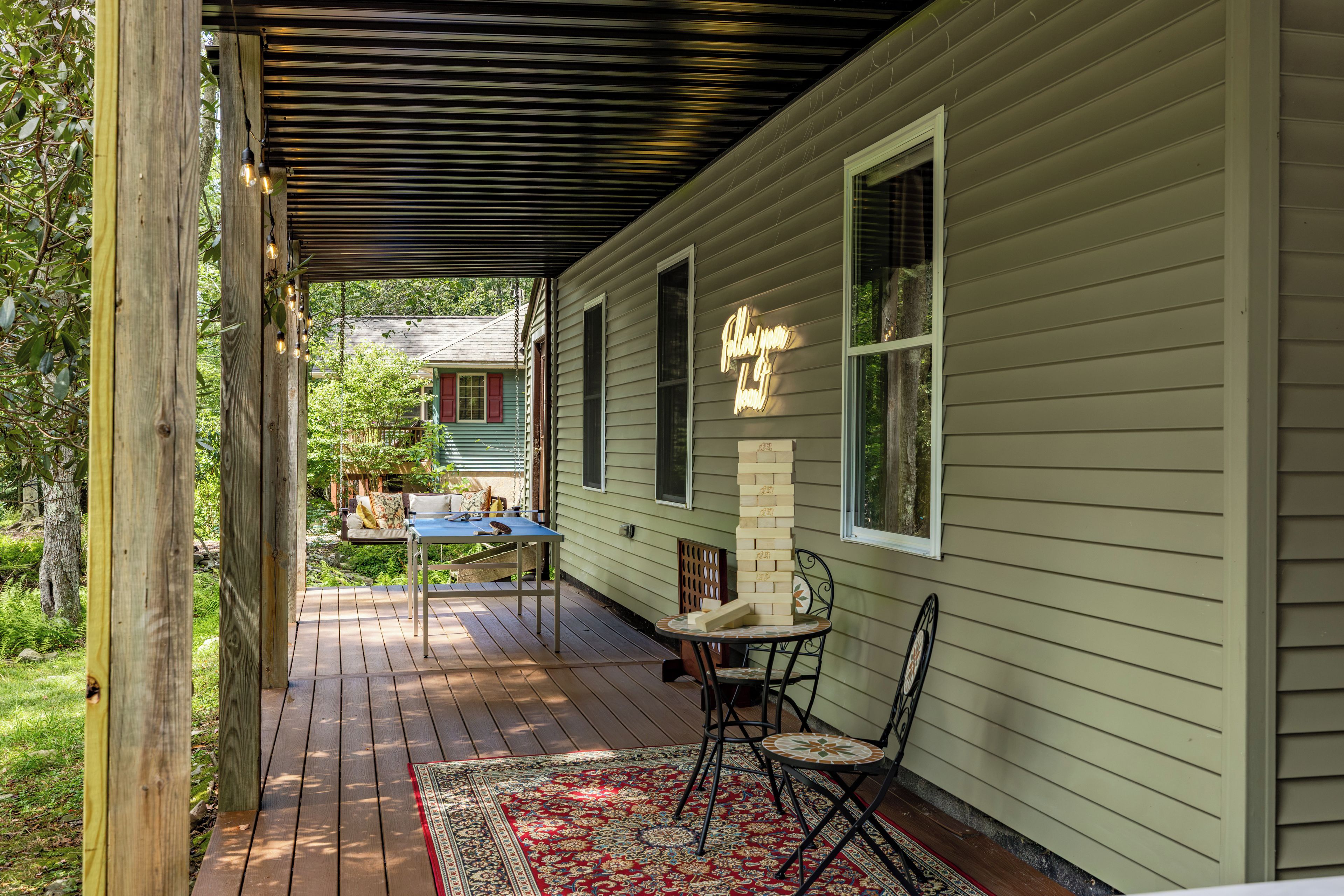 A covered porch with a table and chairs, a hanging light fixture, and a brick wall with a neon sign.