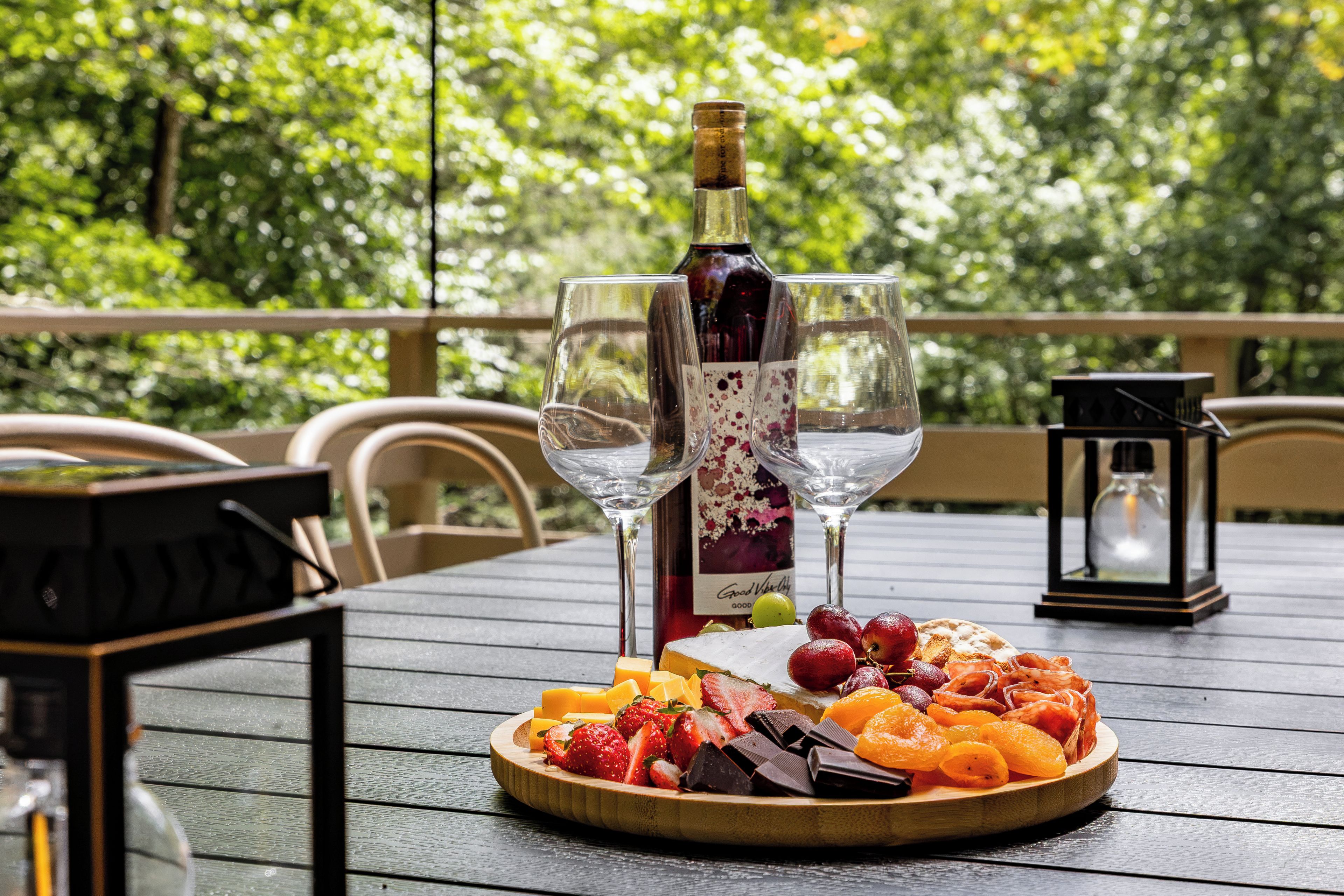 A wooden table with a bottle of wine, two wine glasses, and a fruit platter.