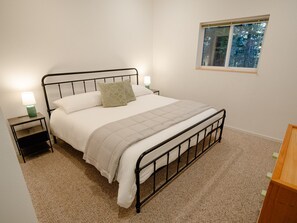 A single bed with a metal frame, two bedside tables with lamps, a window with a view of trees, and a carpeted floor. - The Nook | Modern Redwood Escape Near Gualala (Gualala)