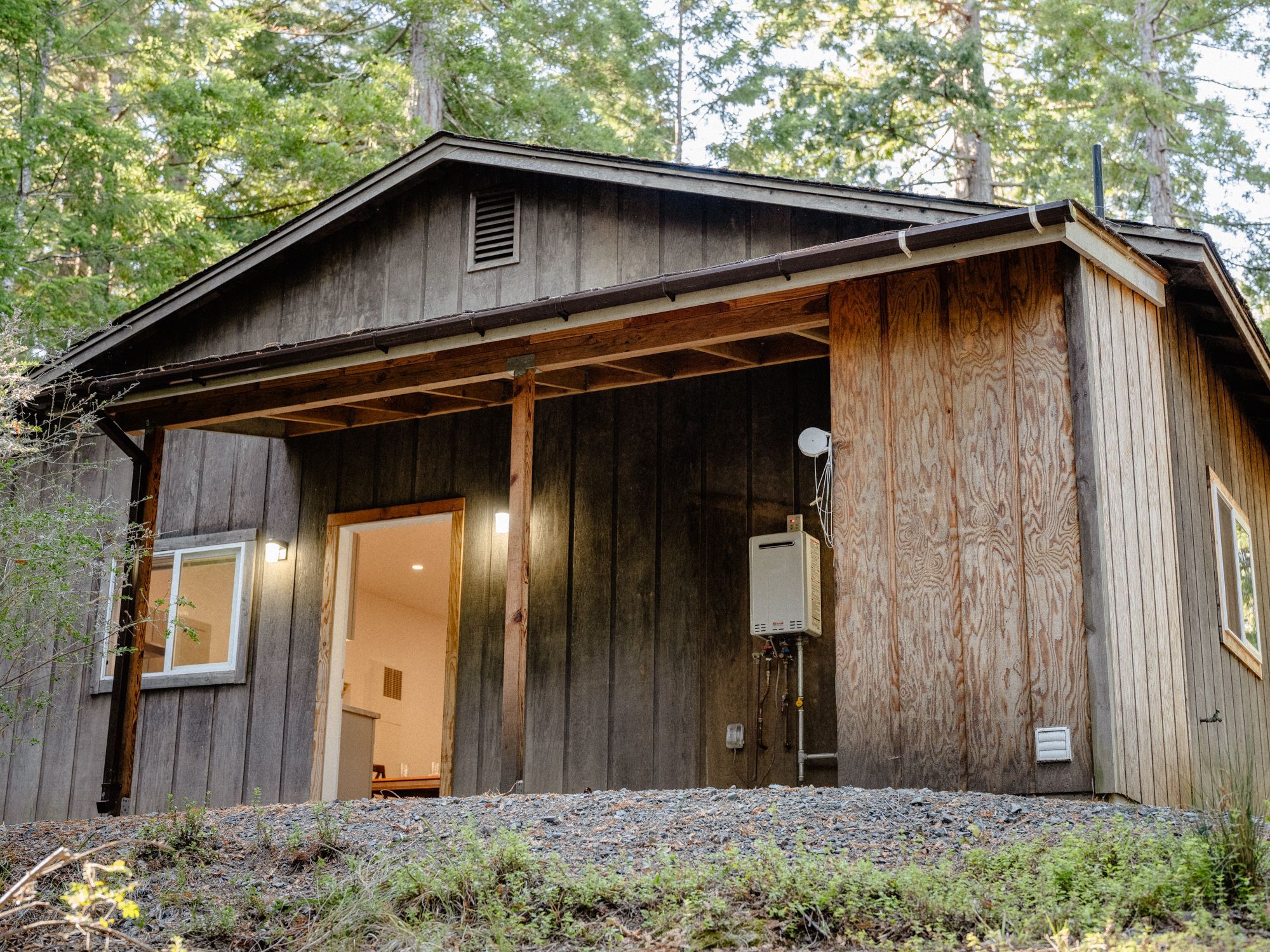 A rustic cabin with a covered porch, a satellite dish, and a visible interior door.