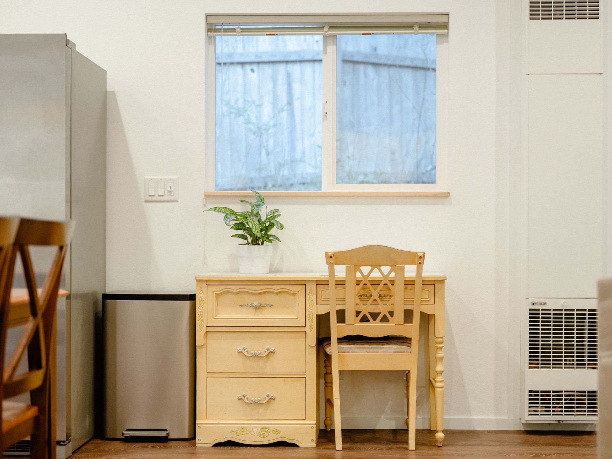 A compact room with a wooden desk, a chair, a small potted plant, and a window with curtains.