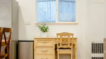 A compact room with a wooden desk, a chair, a small potted plant, and a window with curtains.