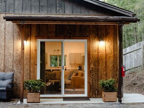 A wooden exterior with a sliding glass door leading to a living area with a couch and a coffee table. - The Nook | Modern Redwood Escape Near Gualala (Gualala)