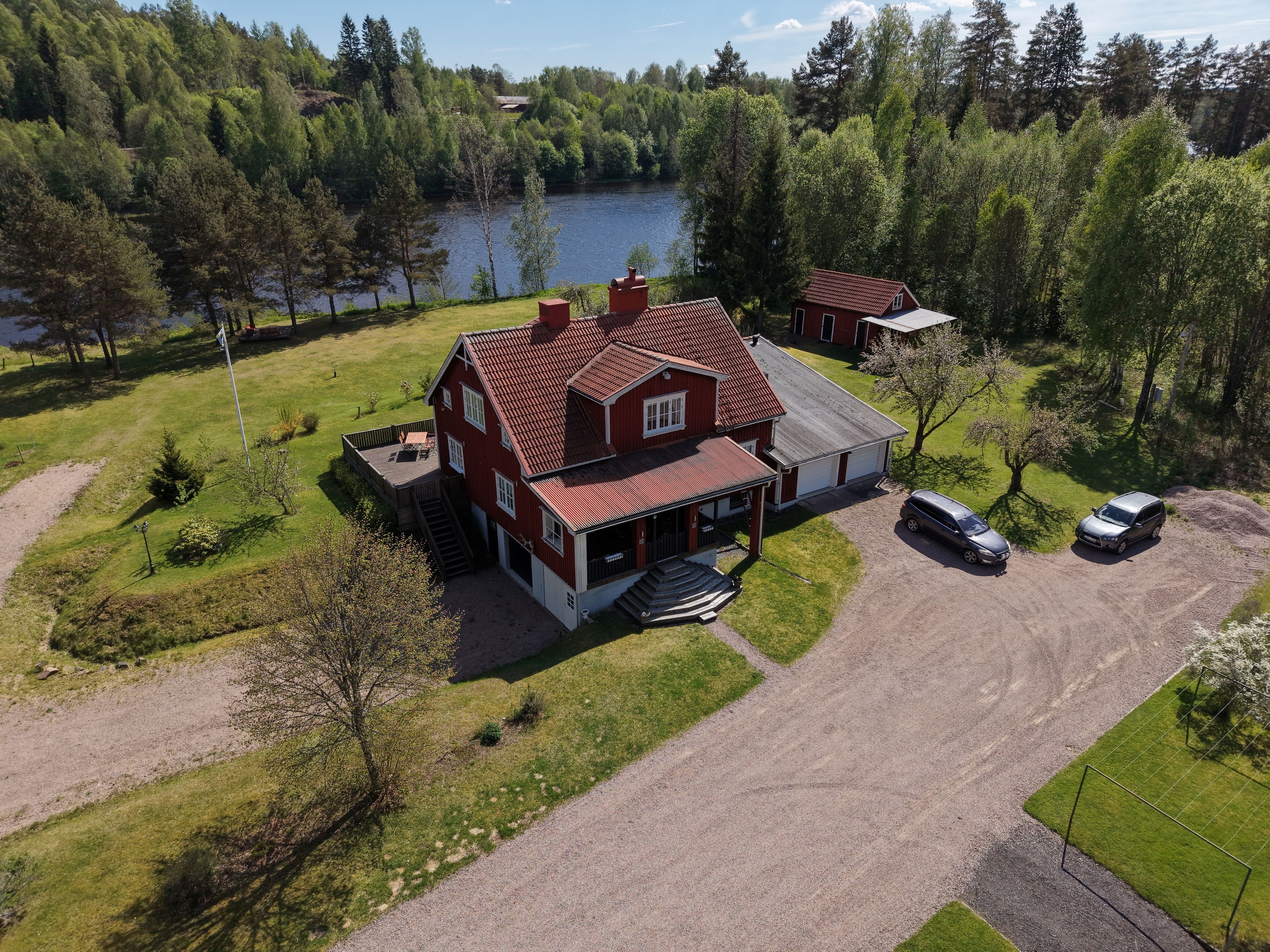 Ett tvåvåningshus med ett rött tak, en uppfart och en sjö i bakgrunden.