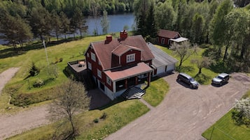 Ett tvåvåningshus med ett rött tak, en uppfart och en sjö i bakgrunden.