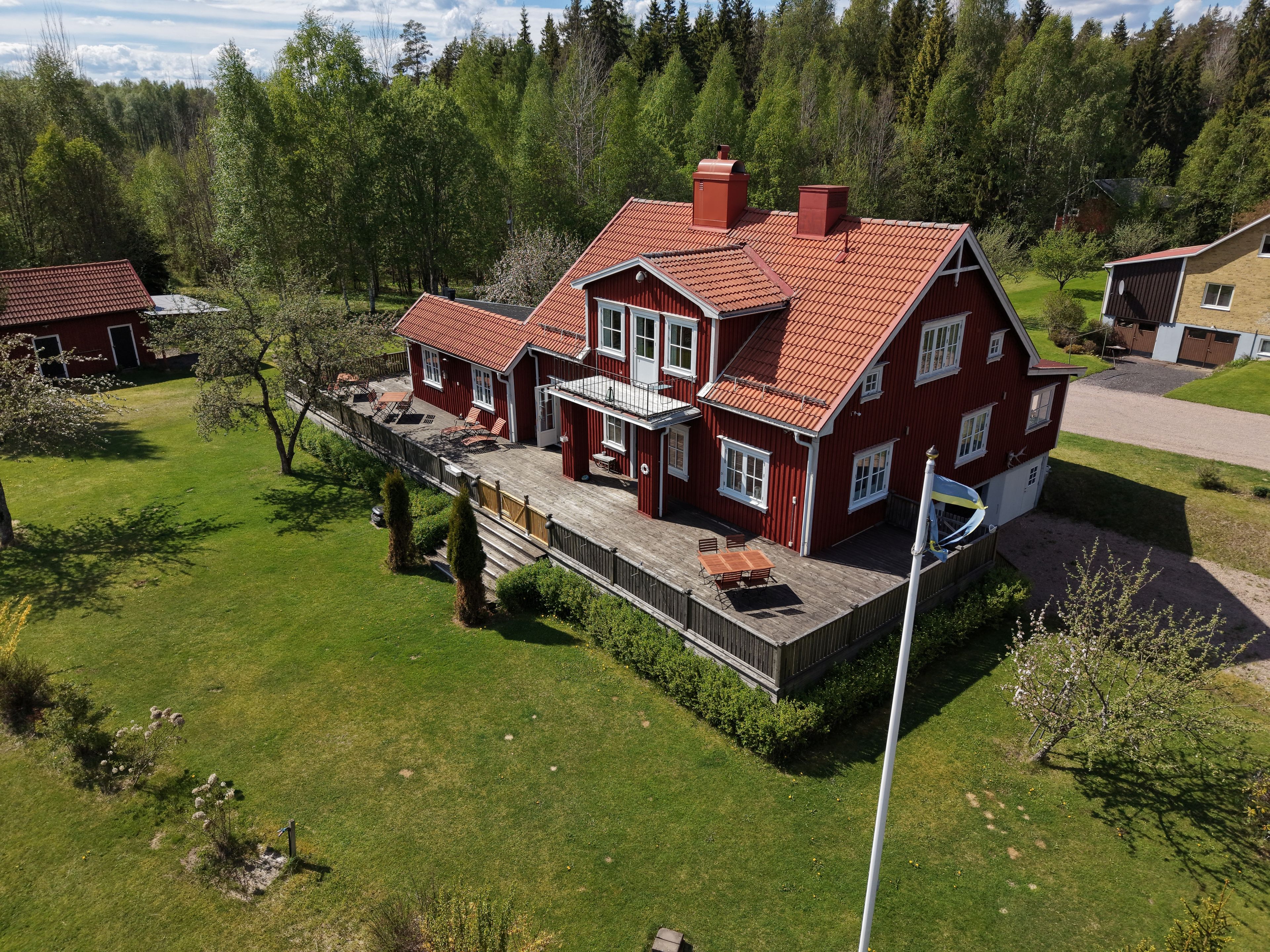 A red house with a balcony, surrounded by a green lawn and trees.