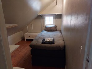 A small, narrow room with a single bed, a nightstand, and a window.