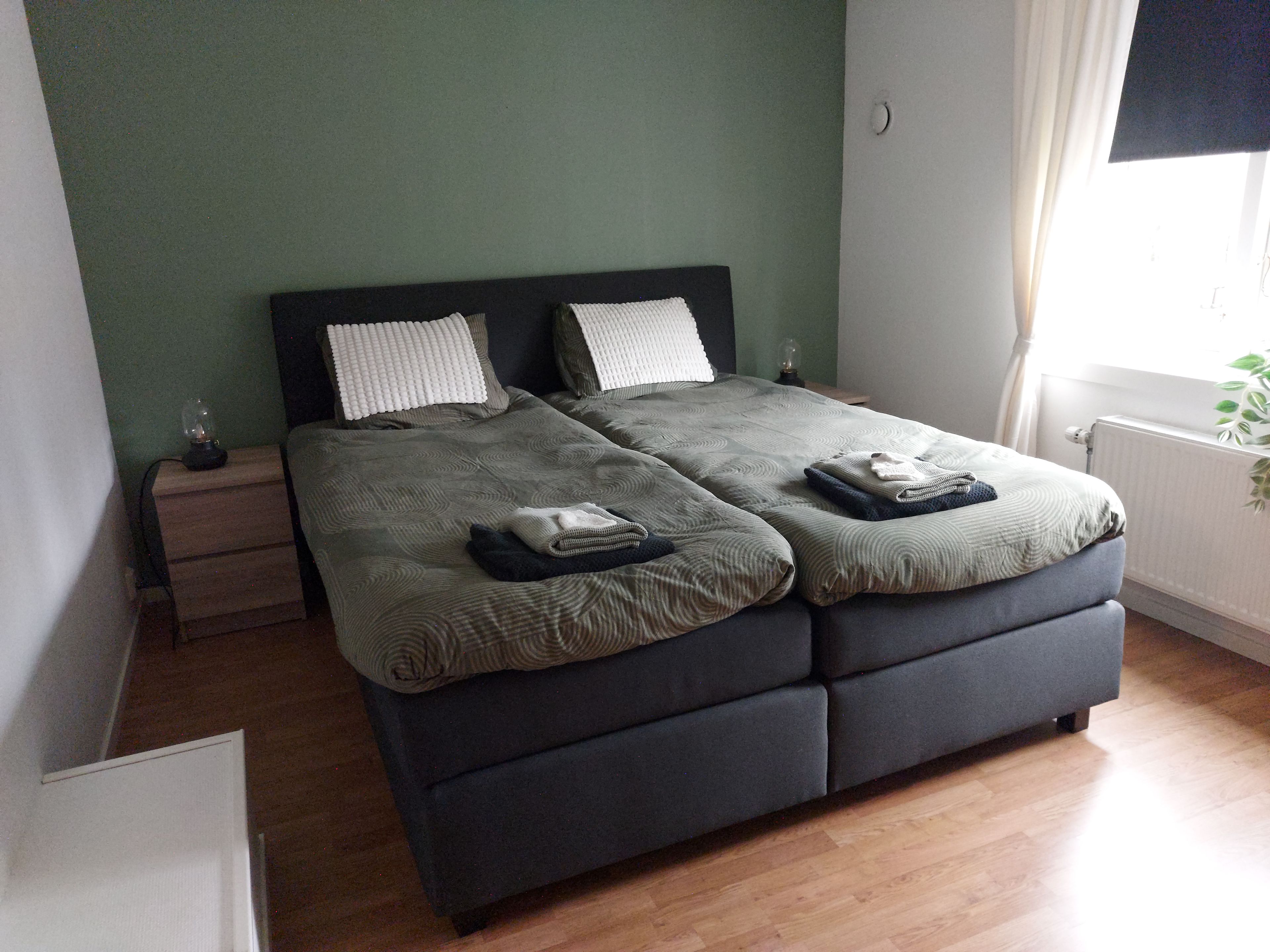 A double bed with a dark headboard, two pillows, and folded blankets on a wooden nightstand.