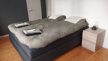 En säng med en mörk sänggavel, ett nattduksbord med en lampa och en dörr i bakgrunden.