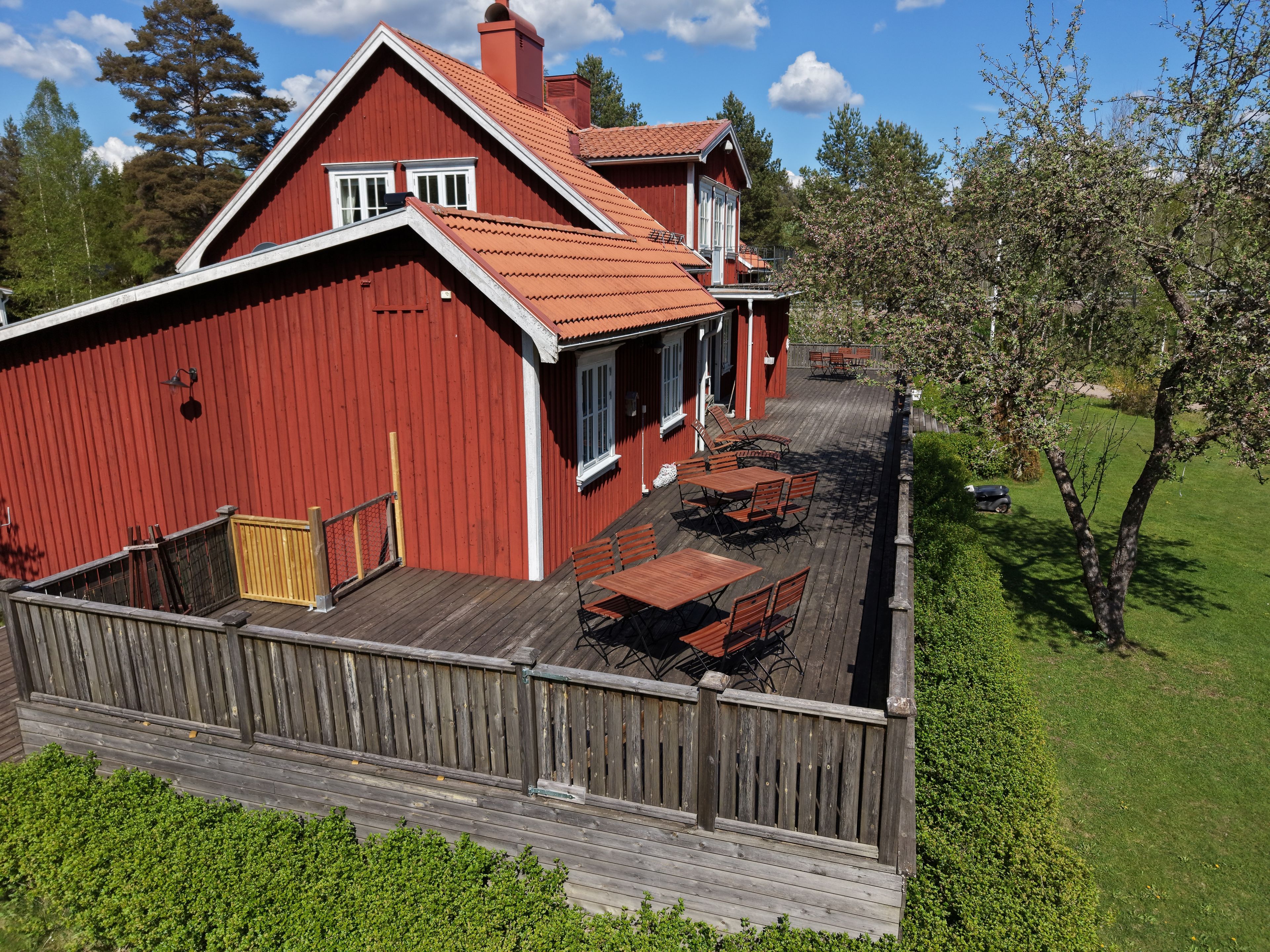 En röd lada med en träveranda och ett utomhusområde med sittplatser.