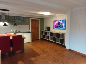 Une pièce dotée d’un plancher en bois, d’une table à manger avec des chaises, d’un coin cuisine avec un évier et des placards, et d’un téléviseur fixé au mur.