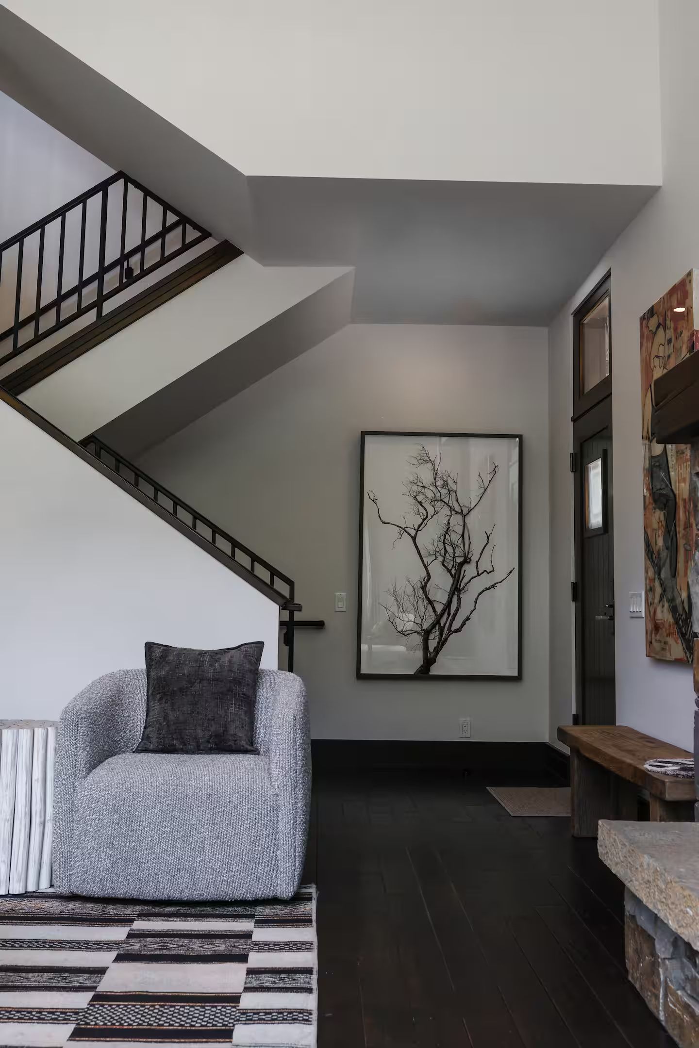 A modern interior with a staircase, a gray sofa, a patterned rug, and a framed artwork of a tree.
