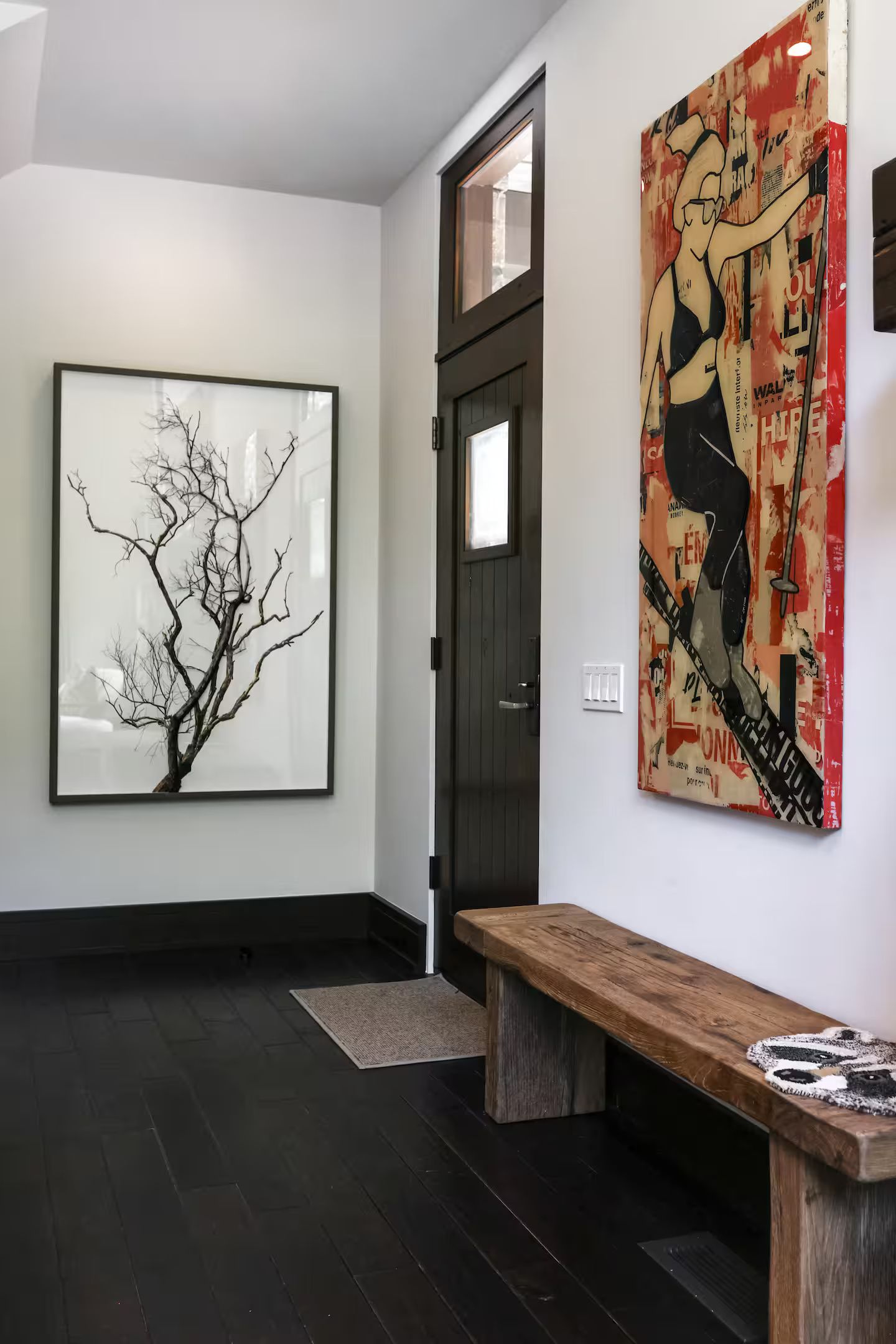 Un couloir avec un banc en bois, un tableau abstrait représentant un arbre encadré et une grande affiche avec une illustration et du texte.