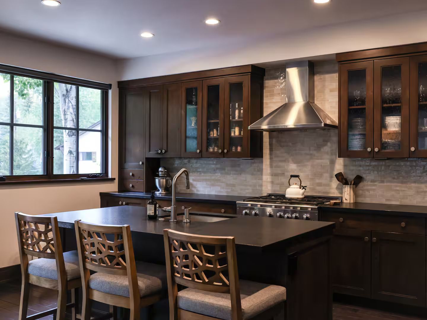 A modern kitchen with dark wood cabinets, a stainless steel range hood, and a large island with seating.