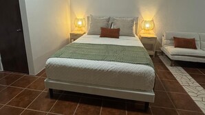 A bedroom with a bed, two bedside tables, a nightstand, a sofa, and a patterned rug. - Bright Studio — Walk to Beach, Town & Ferry in Vieques (Vieques)