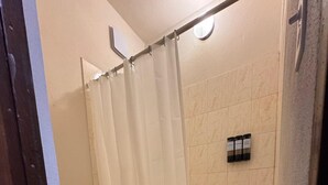 A bathroom with a toilet, a shower with a curtain, and a tiled floor. - Bright Studio — Walk to Beach, Town & Ferry in Vieques (Vieques)