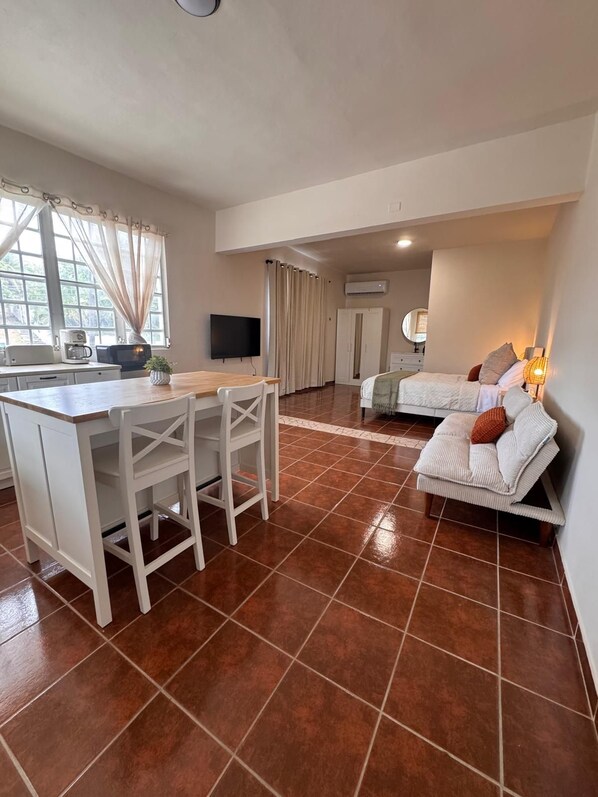 A room with a kitchenette, a dining area, and a bed.