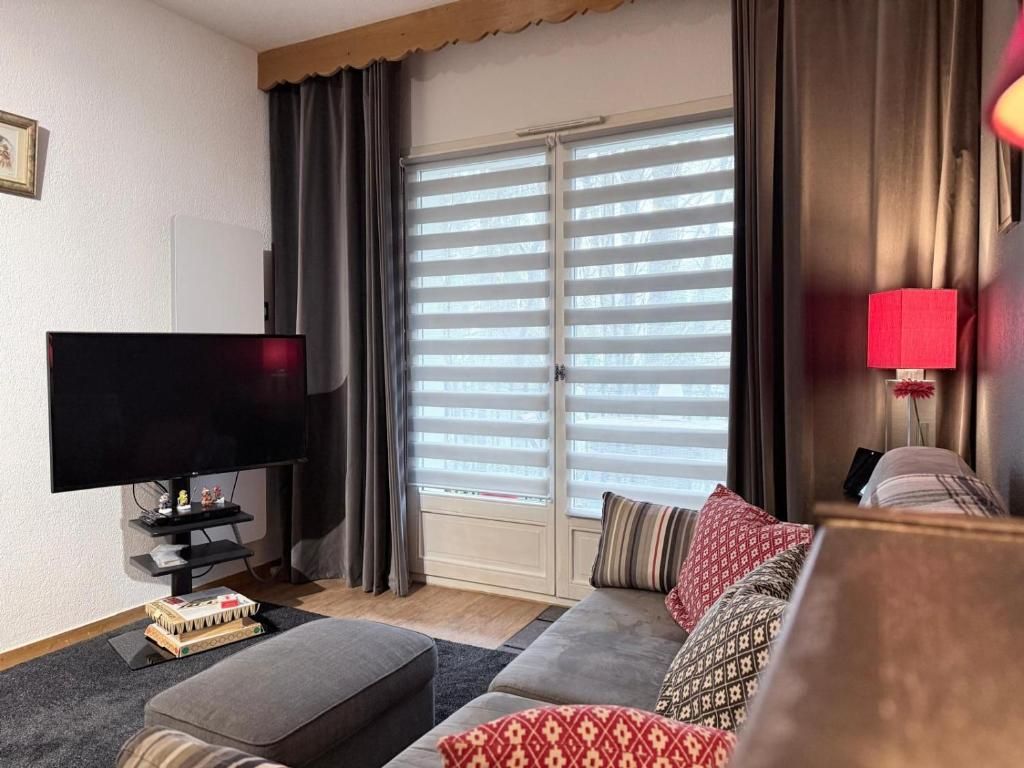 A living room with a flat-screen TV, a sofa, a coffee table, and a window with blinds.