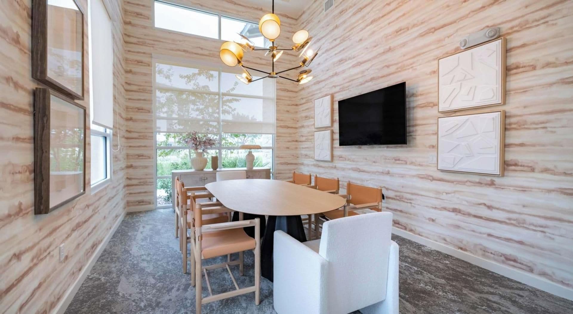 A conference room with a round table, chairs, a chandelier, a TV, and framed artwork on the walls.