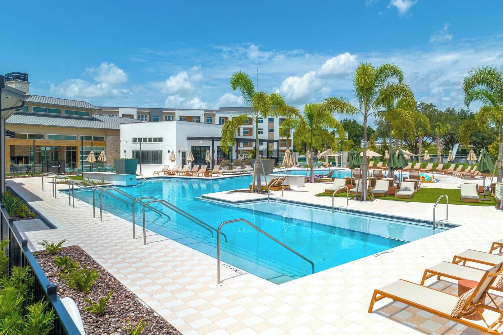 A resort pool area with multiple swimming pools, lounge chairs, and palm trees.