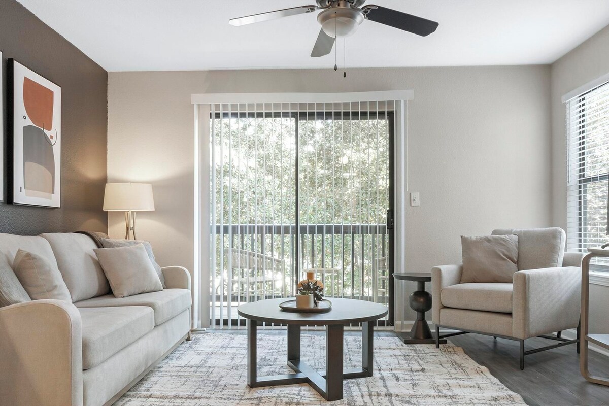A living room with a sofa, armchair, round coffee table, and a ceiling fan.