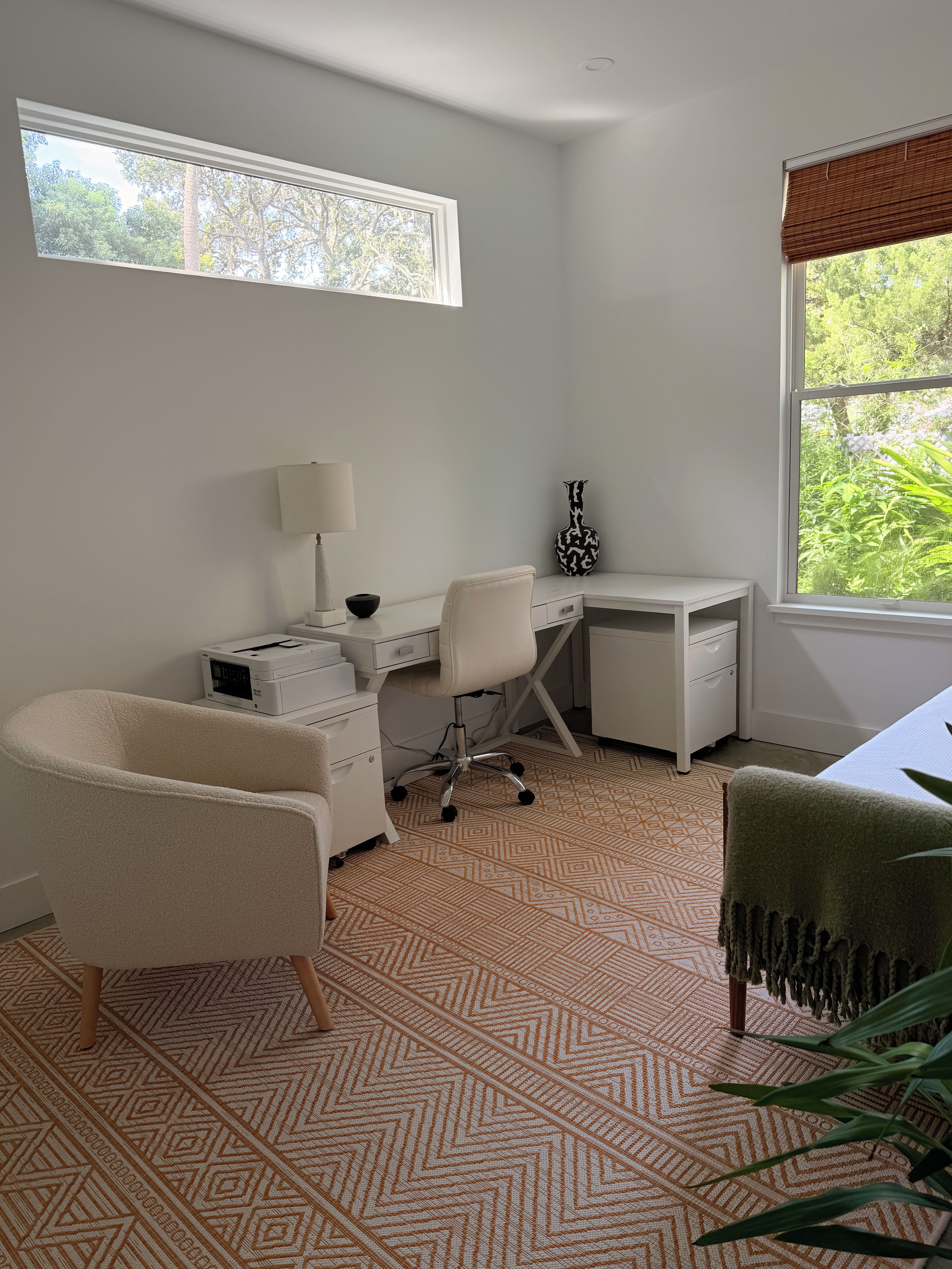 Una habitación con escritorio, silla, lámpara y ventana con vista a follaje.